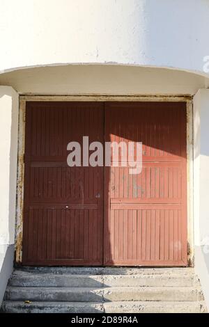 Ein altes verlassene Lagerhaus, ein braunes Tor mit abblätternder Farbe auf hellem Hintergrund. Heller Hintergrund der Wand. Rustikaler Stil Stockfoto