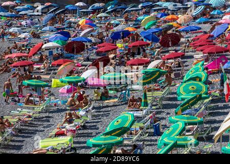 Camogli, Italien. 21. August 2020: Italienischer Strand mit zahlreichen Touristen auf einem Strandurlaub in Italien. Bunte Sonnenschirme und Liegestühle im Sommer. Stockfoto