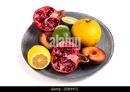 Mandarine, Limette, Zitrone, Granatapfel und Pflaume auf einer grauen Schale isoliert auf weißem Hintergrund. Frische Sommerfrüchte Zusammensetzung. Stockfoto