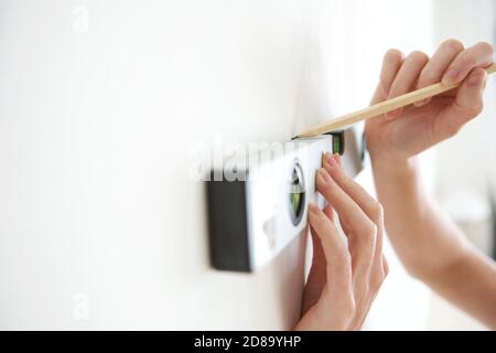 Nahaufnahme der weiblichen Hände mit Wasserwaage und Bleistift Zum Markieren einer geraden Linie an der Wand Stockfoto