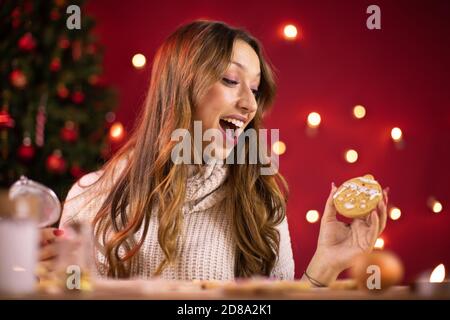 Fröhliche Frau macht Weihnachtsbäckerei, sieht auf selbstgemachten Plätzchen mit Freude Stockfoto