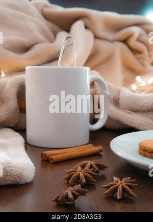 Wohnzimmer Details im Winter. Nahaufnahme einer weißen Tasse mit einer Infusion auf einem Holztisch mit Anis und Zimt und einer cremefarbenen Decke. Heimelig Stockfoto