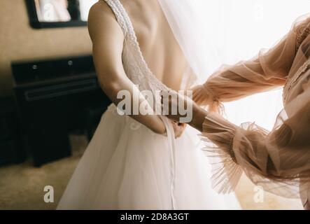 Mama hilft Tochter setzen auf Hochzeitskleid Stockfoto