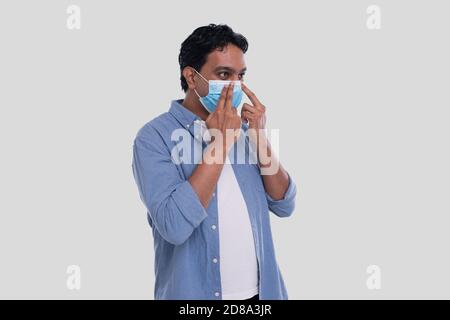 Indischer Mann setzt auf medizinische Maske isoliert. Mann in blauem Hemd zeigt, wie man auf medizinische Maske setzen. Gesundheit, Virus, Medizinisches Konzept Stockfoto