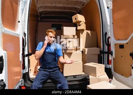 Lader spricht auf dem Smartphone, während er in der Nähe von Paketen im LKW sitzt Im Freien Stockfoto