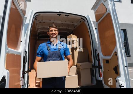 Lader in Overalls halten Paket in der Nähe von LKW auf der städtischen Straße Stockfoto