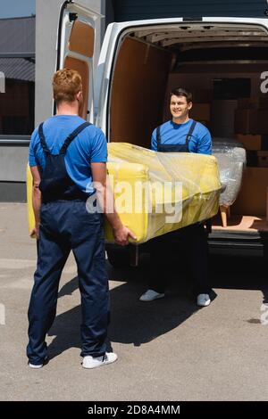Selektive Fokussierung des Laders, der den Tisch in Stretchfolie mit trägt Kollege in der Nähe von LKW auf der städtischen Straße Stockfoto
