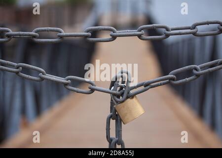 Starke Kette mit Vorhängeschloss blockiert den Weg zu einer Holzbrücke. Nahaufnahme des Bildes mit selektivem Fokus und geringer Schärfentiefe. Stockfoto