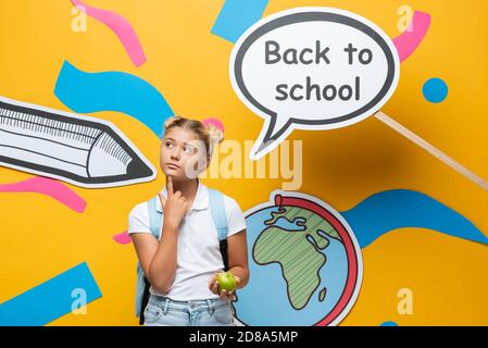 Nachdenkliches Schulkind mit Apfel und Rucksack in der Nähe von Papier Rede stehen Blase mit Rücken zur Schule Schriftzug auf gelbem Hintergrund Stockfoto