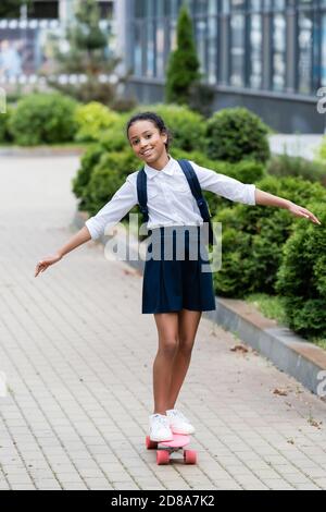 Happy african american Schulmädchen mit Rucksack Reiten Penny Board im Freien Stockfoto