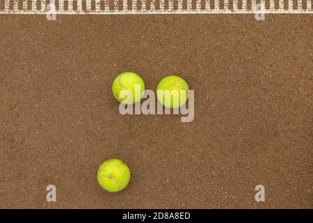 Drei Tennisbälle liegen nebeneinander auf einem roten Sandplatz. Blick von oben. Stockfoto