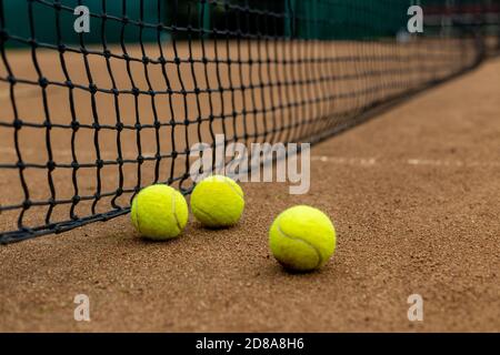 Drei Tennisbälle liegen nebeneinander auf einem roten Sandplatz entlang des Spielnetzes. Stockfoto