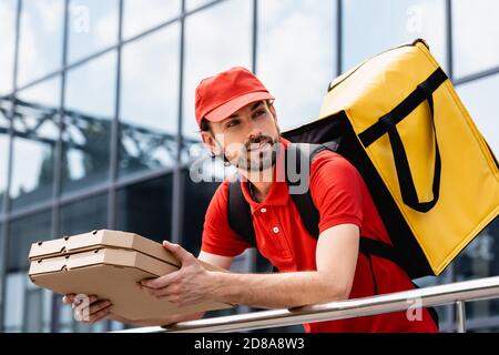 Der Lieferer hält Pizzaboxen in der Nähe des Geländers auf der städtischen Straße Stockfoto