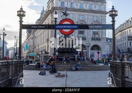 Ein Straßenmusiker spielt Gitarre am Piccadilly Circus unter einem Londoner U-Bahn-Schild an einem sonnigen Nachmittag. London Stockfoto