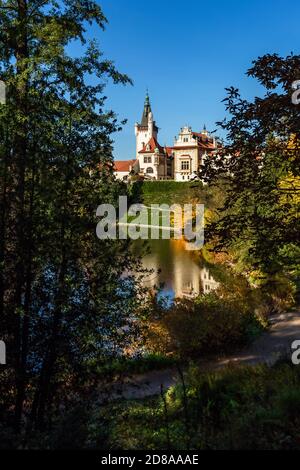 Pruhonice, Tschechische Republik - Oktober 25 2020: Blick auf die romantische Burg durch grüne Bäume auf einem hil in einem Park. Reflexion im Wasser. Stockfoto