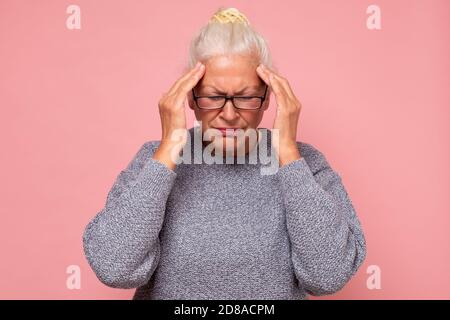 Ältere Frau, die ihre Hände an ihre Schläfen hält und schreckliche Kopfschmerzen hat. Stockfoto