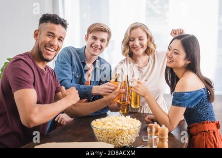 Fröhliche multikulturelle Freunde Blick auf die Kamera, während klickende Flaschen von Bier Stockfoto