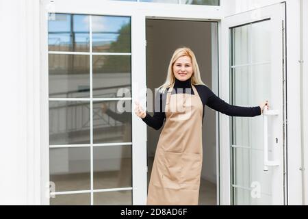 Halbe Länge Porträt der Kellnerin in Schürze gekleidet mit Kopieplatz für Markennamen Open Store Start Arbeit bereit, Besucher zu dienen, Frau Unternehmer Stockfoto