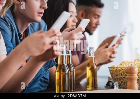 Selektiver Fokus von multiethnischen Freunden chatten auf Smartphones in der Nähe von Bier Während der Party Stockfoto