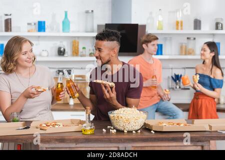 Multiethnische Freunde klirren Flaschen Bier während Pizza halten während Party Stockfoto