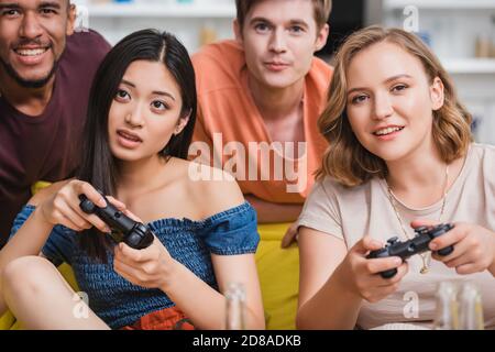 KIEW, UKRAINE - 28. JULI 2020: Selektiver Fokus der konzentrierten multiethnischen Freunde spielen Videospiel während der Party Stockfoto