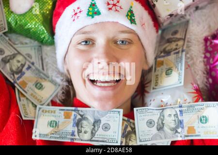 Glückliche Frau mit Geldscheinen bedeckt und umgeben von Geschenken an den Weihnachtsfeiertagen. Stockfoto