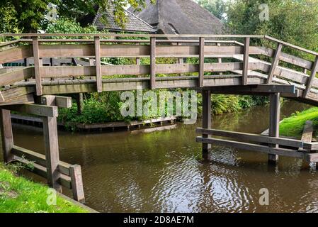 Hölzerne dekorative Fußgängerbrücke über einen Kanal in den Niederlanden im Hintergrund von Pflanzen und Gebäuden. Stockfoto