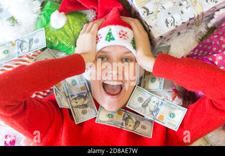 Erstaunt aufgeregt junge Frau von Geldscheinen Rechnungen und viele Weihnachtsgeschenke umgeben. Stockfoto