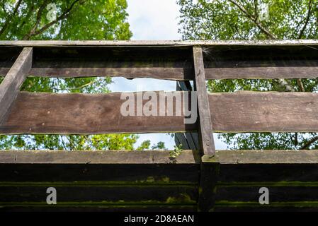 Hölzerne dekorative Fußgängerbrücke über einen Kanal in den Niederlanden im Hintergrund von Pflanzen und Gebäuden. Stockfoto