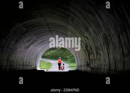 Mutter und Kind, die aus einem dunklen Tunnel in Richtung Ein öffentlicher Park Stockfoto