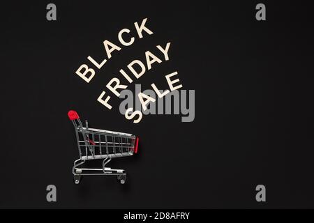 Schwarzer Freitag Verkauf Wort mit Holzbuchstaben über rot Warenkorb auf dunklem Hintergrund gemacht. Shopping, Commerce und Verkaufskonzept. Flach Lay Banner mit Stockfoto