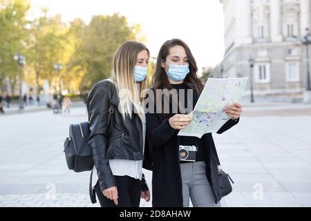 Zwei Freundinnen, die in der Stadt stehen und auf eine Touristenkarte schauen. Sie tragen Gesichtsmasken. Konzept der neuen Normalität. Stockfoto