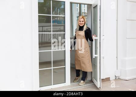 Halbe Länge Porträt der Kellnerin in Schürze gekleidet mit Kopieplatz für Markennamen Open Store Start Arbeit bereit, Besucher zu dienen, Frau Unternehmer Stockfoto