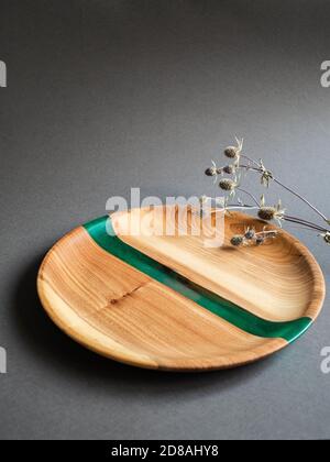 Rundes Holztablett mit grünem Harzeinsatz und trockenen Zweigen auf schwarzem Hintergrund. Vorderansicht. Speicherplatz kopieren Stockfoto