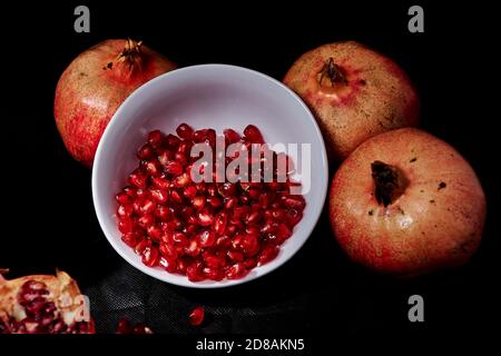 Granatäpfel um weiße Schale mit Samen, schwarzer Hintergrund, Makrofotografie Stockfoto