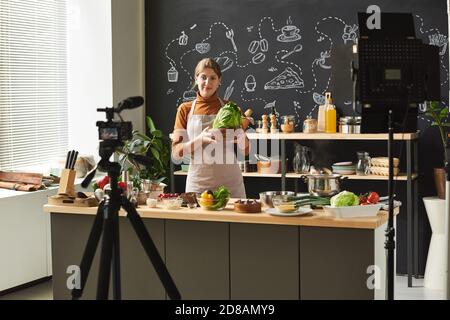 Junge Lebensmittel-Bloggerin hält Gemüse in den Händen Aufnahme ein Video über die Kamera Sie betreibt ihren Blog Stockfoto