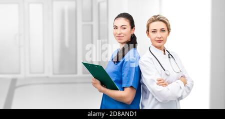 Ärztin und Krankenschwester, die gemeinsam im Krankenhaus in die Kamera schauen. Medizinisches Team steht über einer Korridorklinik Stockfoto