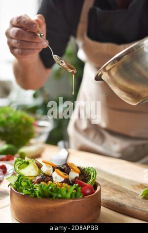 Nahaufnahme des Küchenchefs, der Sojasauce in das Gericht mit Fleisch eingibt Und Gemüse am Tisch Stockfoto