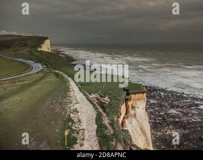 Eastbourne, East Sussex, Großbritannien. Oktober 2020. Dunkler Himmel und sintflutartiger Regen über den Kreidefelsen. Beachy Head Leuchtturm in der Ferne. Während die Erosion zunimmt, während die Kreide weich wird, hängt dieser große Brocken immer noch an. Die Öffentlichkeit wird erneut vor der extremen Fragilität der Klippen mit erhöhtem plötzlichem Gesteinsfallrisiko gewarnt. Der Fotograf verwendete die entsprechende Ausrüstung und war nicht am Rand. Kredit: David Burr/Alamy Live Nachrichten Stockfoto