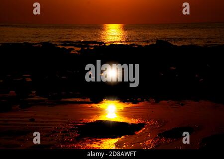 Orange gelb golden lebhafter Sonnenuntergang auf tropischer Insel über Ebbe Ozean mit Spiegelung des Sonnenstrahls im Wasser und Sunburst-Effekt - Thailand, Ko Lan Stockfoto
