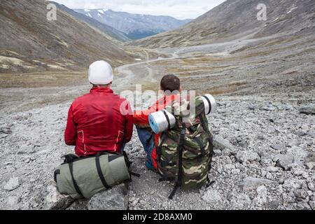 Zwei Rucksacktouristen sitzen auf Steinen und blicken in die Ferne, der einzige Weg durch das Tal Stockfoto