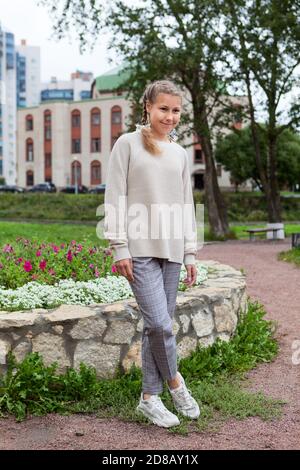 In voller Länge Porträt von Pre-teen kaukasischen Mädchen tragen beige Bluse und graue Hosen stehen im Freien, posiert für die Kamera Stockfoto