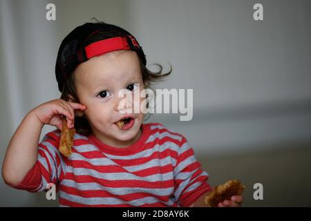 Ein kleiner Junge, der Toast in einer Mütze und gestreiftem Oberteil isst. ©PRWPhotography Stockfoto