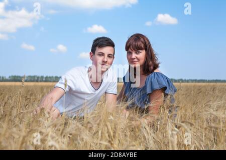 Erwachsene Mutter mit ihrem Sohn im Teenageralter sitzt in gelben Weizenfeldern, zwei kaukasische Menschen Stockfoto