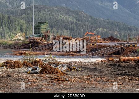 Logs Rampe. Holzstämme aus Kiefernwäldern in einem Haufen im Dorf Sayward in Kanada mit Bergen im Hintergrund gestapelt. Selektiver Fokus. Stockfoto