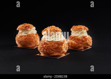 Nahaufnahme von Hree köstliche frische profiteroles mit süßen weißen Creme im Inneren. Hausgemachte leckere Eclare isoliert auf schwarzem Studio-Hintergrund. Konzept der Desserts, Restaurant Essen. Stockfoto