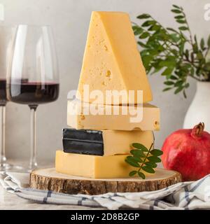 Verschiedene Käsesorten mit Gläsern Rotwein und Granatapfel auf einem Leinentischtuch. Stockfoto