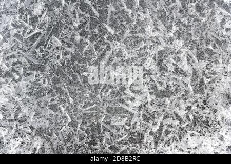 Eine Nahaufnahme des Eises auf der Oberfläche eines gefrorenen Sees. Das Eis ist geknackt und strukturiert. Schwarz und Weiß. Stockfoto