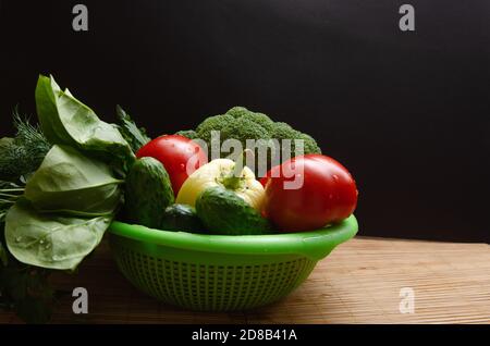 Gemüsemischung von Tomaten, Gurken, Kräutern, Brokkoli, auf einem Teller auf dunklem Grund. Freier Speicherplatz für Text Stockfoto