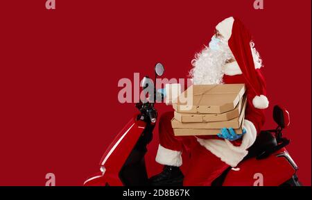 Ältere Santa in einer Schutzmaske und Handschuhe auf einem Retro-Motorrad liefern Fast Food und Pizza während der Coronavirus Quarantäne. Zeigen zum l Stockfoto